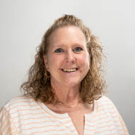 A woman smiling in a striped shirt against a plain gray background.